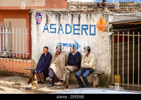 1 chien, colombien 3 hommes, 1 femme assis sur le banc, en attente. 1 dans le poncho traditionnel à chapeau, Ruana. Asadero signe Boyacá département, Colombie, Amérique du Sud Banque D'Images