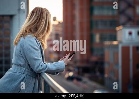 Femme tenant un smartphone et attendant l'appel. Fond urbain. Femme d'affaires debout sur la terrasse et donnant sur la rue de la ville Banque D'Images