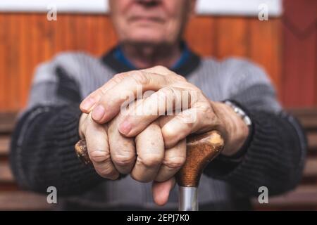 Homme âgé tenant une canne à pied dans la main. Vieux pensionné assis sur le banc et relaxant. Processus de vieillissement et problème d'incapacité Banque D'Images