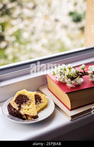Tranche de gâteau, livres et fleurs sur parapet. Vue depuis la fenêtre de l'arbre en fleurs. Profitez d'un rafraîchissement au printemps Banque D'Images