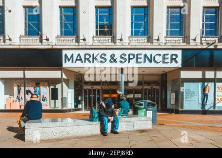 Les gens s'assoient sur un banc de marbre devant le magasin Marks & Spencer de Broad Street à Reading, au Royaume-Uni. Le magasin est fermé à un verrouillage causé par COVID. Banque D'Images