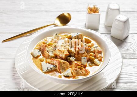 Cuisine allemande : ragoût de porc à la crème, cornichons et fromage bleu, paprika fumé servi sur une assiette blanche avec une cuillère dorée sur un dos en bois blanc Banque D'Images