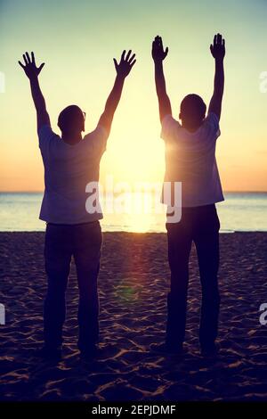 Ton de la silhouette de deux hommes avec les mains vers le haut à L'arrière-plan du coucher du soleil Banque D'Images