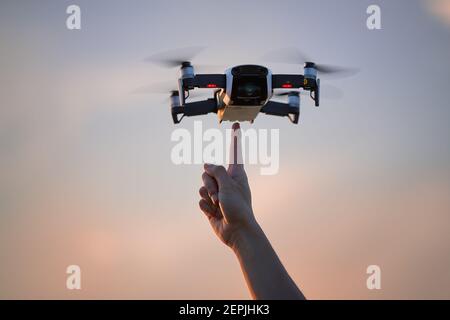 Un petit modèle de quadcopter planant dans l'air directement au-dessus d'un doigt pointant contre le ciel coloré du soir. Jeune femme qui teste de nouvelles technologies. Banque D'Images