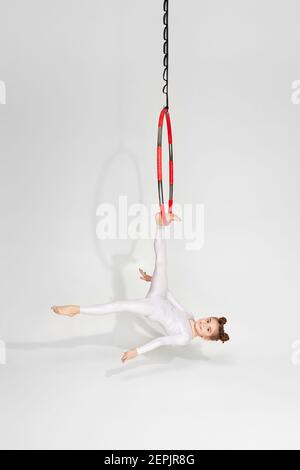 le gymnaste de petite fille en vêtements de sport blancs montre un acrobatique performances sur un arceau aérien Banque D'Images