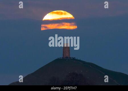 Glastonbury, Somerset, Royaume-Uni. 27 février 2021. Météo Royaume-Uni. La pleine lune de neige s'élève de derrière une couche de nuages à Glastonbury Tor dans le Somerset au crépuscule. Crédit photo : Graham Hunt/Alamy Live News Banque D'Images