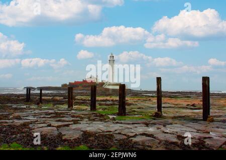 De vieux ponton se dresse sur la rive rocheuse, devant le phare de l’île St. Mary’s, sur la côte de Whitley Bay, en Tyne et en Wear, en Angleterre Banque D'Images