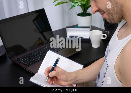 Un gros plan montre l'employé qui remplit les entrées dans le calendrier du livre à l'aide d'un stylo. Travail à distance pendant une pandémie. Un salon lumineux dans un style moderne avec un espace préférable. Banque D'Images