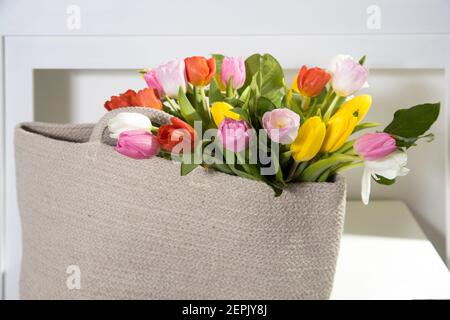 Bouquet de tulipes multicolores dans un sac en rotin blanc sur la table à l'intérieur. Banque D'Images