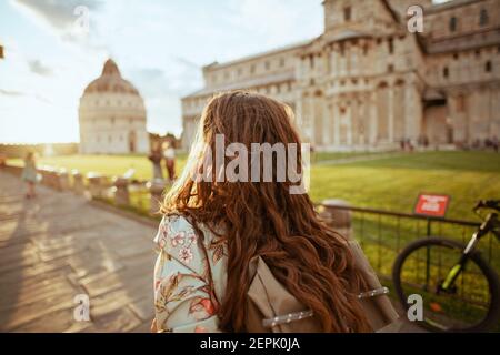 Vue de derrière une élégante femme de voyage solo en robe florale avec sac à dos ayant l'excursion près de Duomo di Pisa. Banque D'Images