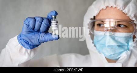 Vaccin contre le coronavirus dans la main du médecin, infirmière en costume d'EPI médical tenant une bouteille de vaccin COVID-19, femme médecin masque regarde le médicament. Concept de c Banque D'Images