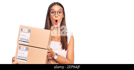 Jeune femme hispanique tenant le paquet de livraison effrayée et stupéfait avec la bouche ouverte pour la surprise, incrédulité visage Banque D'Images