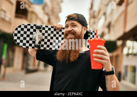 Jeune patineur irlandais tenant du skate et buvant du soda à la ville. Banque D'Images