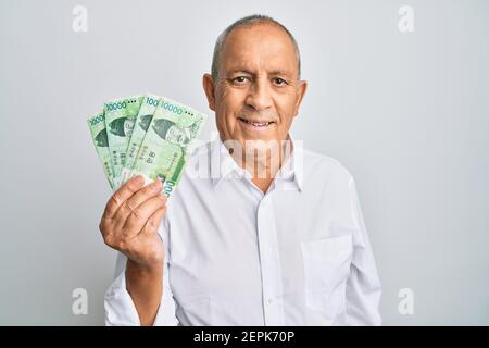 Le beau homme senior détenant 10000 sud-coréens a gagné la recherche de billets une position positive et heureuse et un sourire plein d'assurance affichage des dents Banque D'Images
