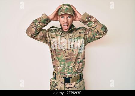 Jeune homme caucasien portant l'uniforme militaire de camouflage fou et effrayé avec les mains sur la tête, peur et surpris de choc avec la bouche ouverte Banque D'Images