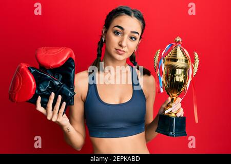 Jeune fille brune tenant des gants de boxeur et trophée détendu avec une expression sérieuse sur le visage. Simple et naturel regarder l'appareil photo. Banque D'Images