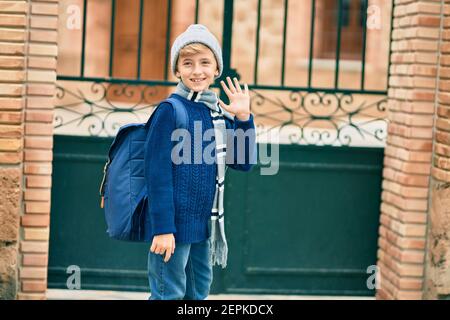 Adorable enfant blond étudiant disant Au revoir avec la main se mettre à l'école. Banque D'Images