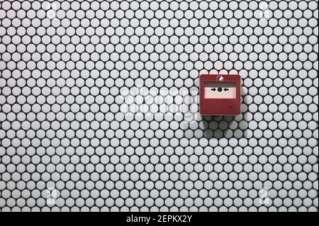 détail d'un bouton d'incendie rouge sur un rond blanc mur de carreaux dans un espace public Banque D'Images