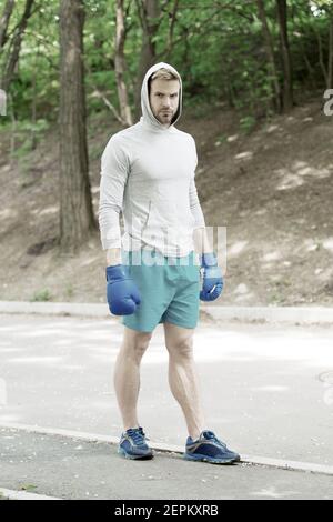Grand jour arrive. Athlète homme concentré sur le visage avec des gants de boxe sport pratique prêt punch fond nature. Boxer hooded motivé pour réussir. Boxer sportif formation avec des gants de boxe. Banque D'Images