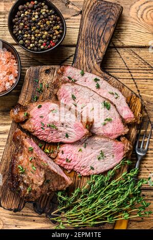Tranches rares de rôti de boeuf sirloin à trois pointes steak bbq sur une planche à découper en bois. fond en bois. Vue de dessus Banque D'Images