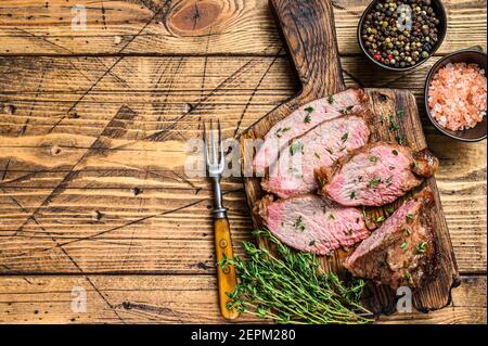 Tranches rares de rôti de boeuf sirloin à trois pointes steak bbq sur une planche à découper en bois. fond en bois. Vue de dessus. Copier l'espace Banque D'Images