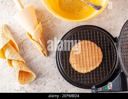 Image plate de l'appareil à gaufrer conique anti-adhésif pour faire des cornets de glace faits maison. Des cônes fraîchement roulés à la main sont posés sur un comptoir en marbre. Ingredien Banque D'Images