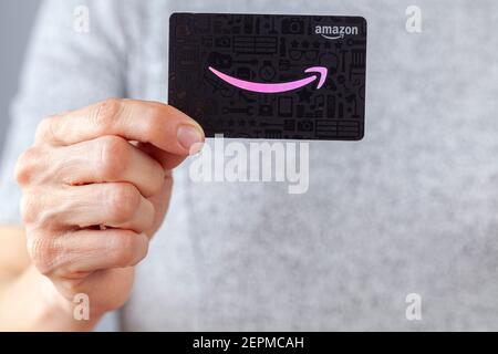 Clarksburg, Maryland, Etats-Unis 02-25-2021: Une femme caucasienne tient une carte-cadeau de Amazon.com (fond noir avec logo rose). Une idée de cadeau polyvalente populaire Banque D'Images