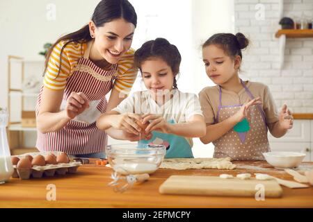 Une mère heureuse et des petites filles curieuses qui font de la pâte pour les biscuits dans la cuisine