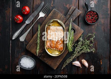 Saumon sauvage de l'Alaska ensemble de poisson fumé en conserve, sur planche à découper en bois, sur fond de table en bois sombre avec herbes et ingrédients, vue du dessus plat Banque D'Images