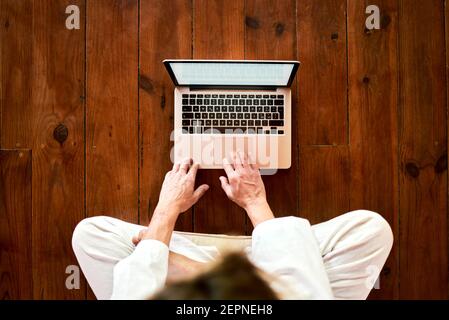 D'en haut court non reconnaissable mâle concentré assis avec des jambes croisées navigation sur netbook dans la salle de méditation tout en pratiquant le yoga Banque D'Images