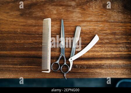 Vue de dessus du ciseaux et du peigne près du rasoir droit avec lames métalliques coupantes sur une table en bois dans le salon de coiffure Banque D'Images