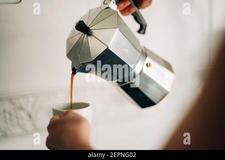 Crop anonyme personne versant le café chaud de métal dessus de cuisinière cafetière dans la cuisine de la maison Banque D'Images