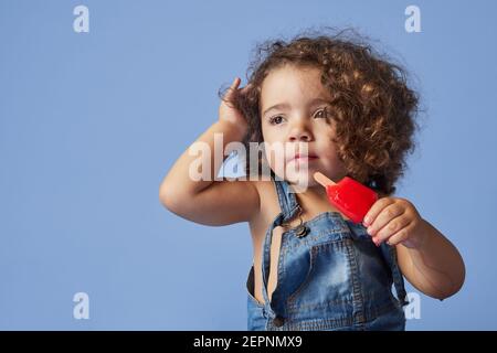 Énervé petite fille regardant loin debout avec de la crème glacée contre arrière-plan studio bleu Banque D'Images