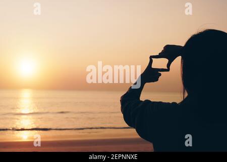 Mise au point sélective des mains de femme faisant un geste de cadre par doigt avec le lever du soleil sur la montagne, Femme capture le lever du soleil ou la lumière du soleil en extérieur. Planification future co Banque D'Images