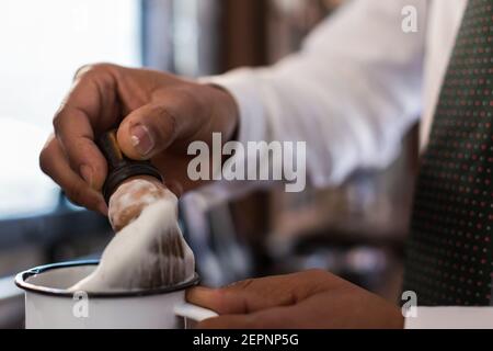 Rognez la brosse coiffante anonyme pour le rasage dans la tasse pendant travailler dans un salon de coiffure Banque D'Images