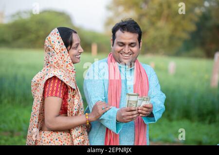 Bon couple de fermiers indiens comptant rupees note au champ d'agriculture, l'homme tenant l'argent. Banque D'Images