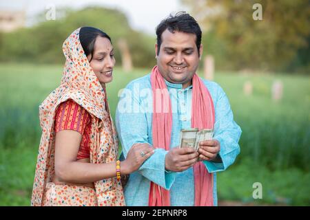 Bon couple de fermiers indiens comptant rupees note au champ d'agriculture, l'homme tenant l'argent. Banque D'Images