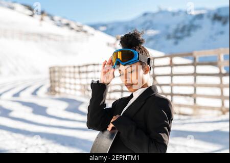 Jolie athlète afro-américaine en tenue tendance et protectrice lunettes debout avec surf des neiges, vue vers le bas en hiver Banque D'Images