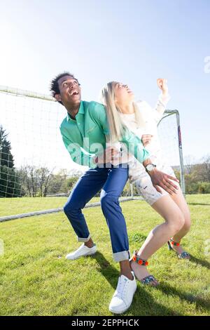 Histoire de football avec un modèle masculin noir et blond Modèle féminin chinois marquant un but sur un terrain de football Banque D'Images