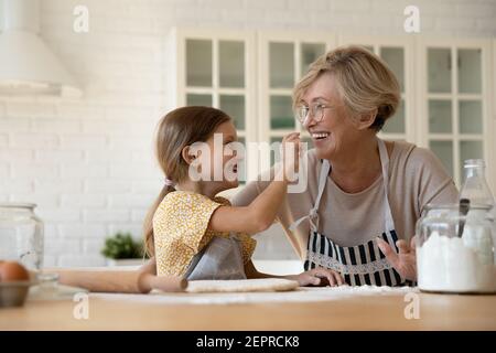 Riant granny âgé et petit-enfant peignant des nez avec de la farine Banque D'Images