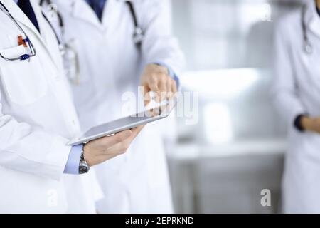 Un groupe de médecins inconnus utilise une tablette pour vérifier certains dossiers médicaux, tout en se tenant dans un bureau d'hôpital. Médecins prêts à Banque D'Images