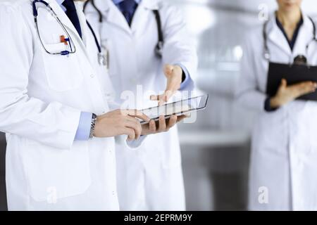 Un groupe de médecins inconnus utilise une tablette pour vérifier certains dossiers médicaux, tout en se tenant dans un bureau d'hôpital. Médecins prêts à Banque D'Images