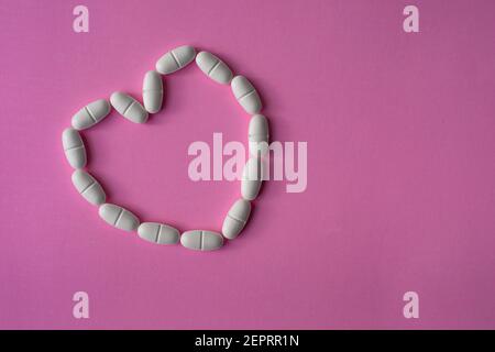 Comprimés ou comprimés blancs, de grande taille, disposés en forme de coeur pour représenter la santé sur fond rose Banque D'Images