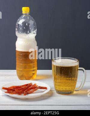 Bière versée dans une tasse en verre d'une bouteille en plastique et des tranches de poisson séché sur une assiette Banque D'Images