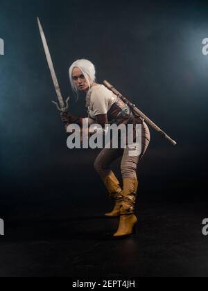 Un jeune guerrier avec une épée sur un fond sombre. Héroïne fantaisie. Jeune belle femme blonde, prête pour la bataille Banque D'Images