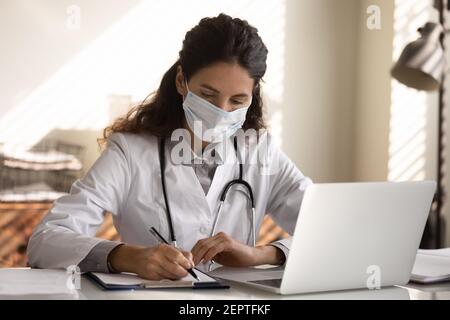 Gros plan médecin femme sérieux portant un masque facial prenant des notes Banque D'Images