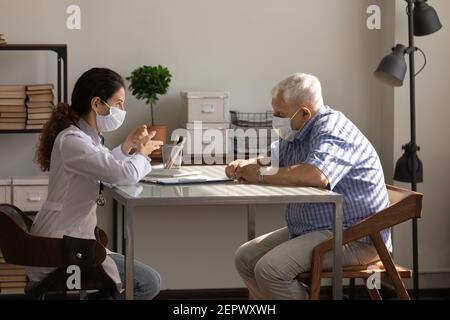 Vue latérale femme médecin portant un masque facial consultant homme âgé Banque D'Images