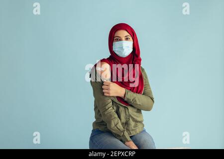 Femme musulmane portant un masque facial de protection montrant son bras avec des aides de bande après avoir reçu la vaccination. La femme présente dans le hijab a reçu le vaccin contre le virus corona. Banque D'Images