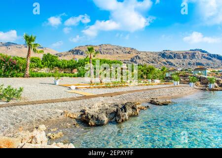 Belle plage rocheuse avec chaises longues et parasols en paille sur la rive de la mer Méditerranée à Rhodes, Grèce Banque D'Images