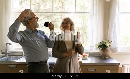Joyeux couple de famille mûre et enthousiaste chantant à ustensiles Banque D'Images